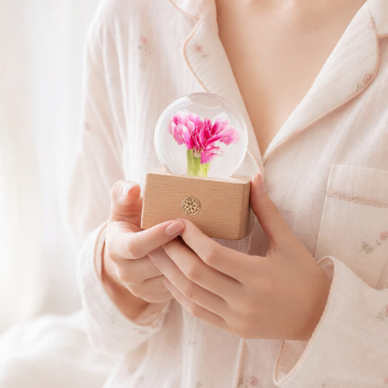 A pink carnation preserved flower lamp held in one hand to show its real size