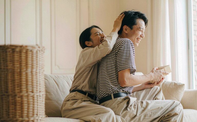 Two friends laughing and hugging as one receives a gift box in a bright living room