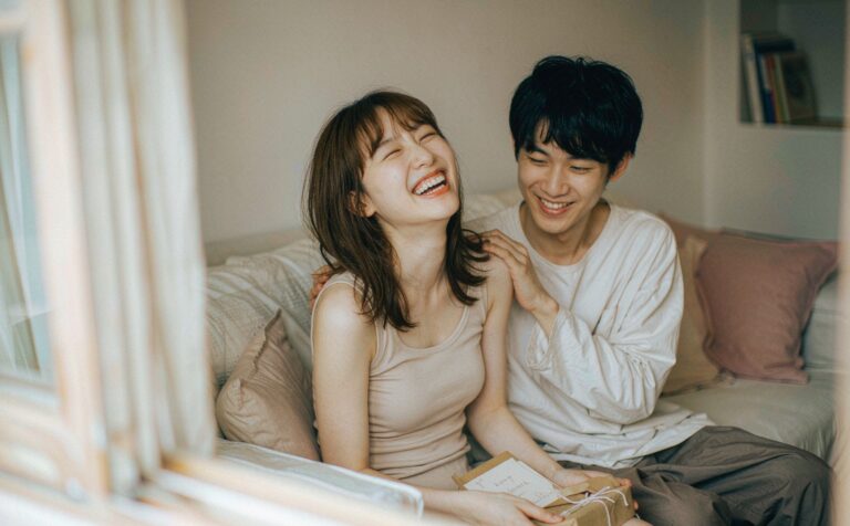 A couple laughing together on a sofa as she unwraps a gift box